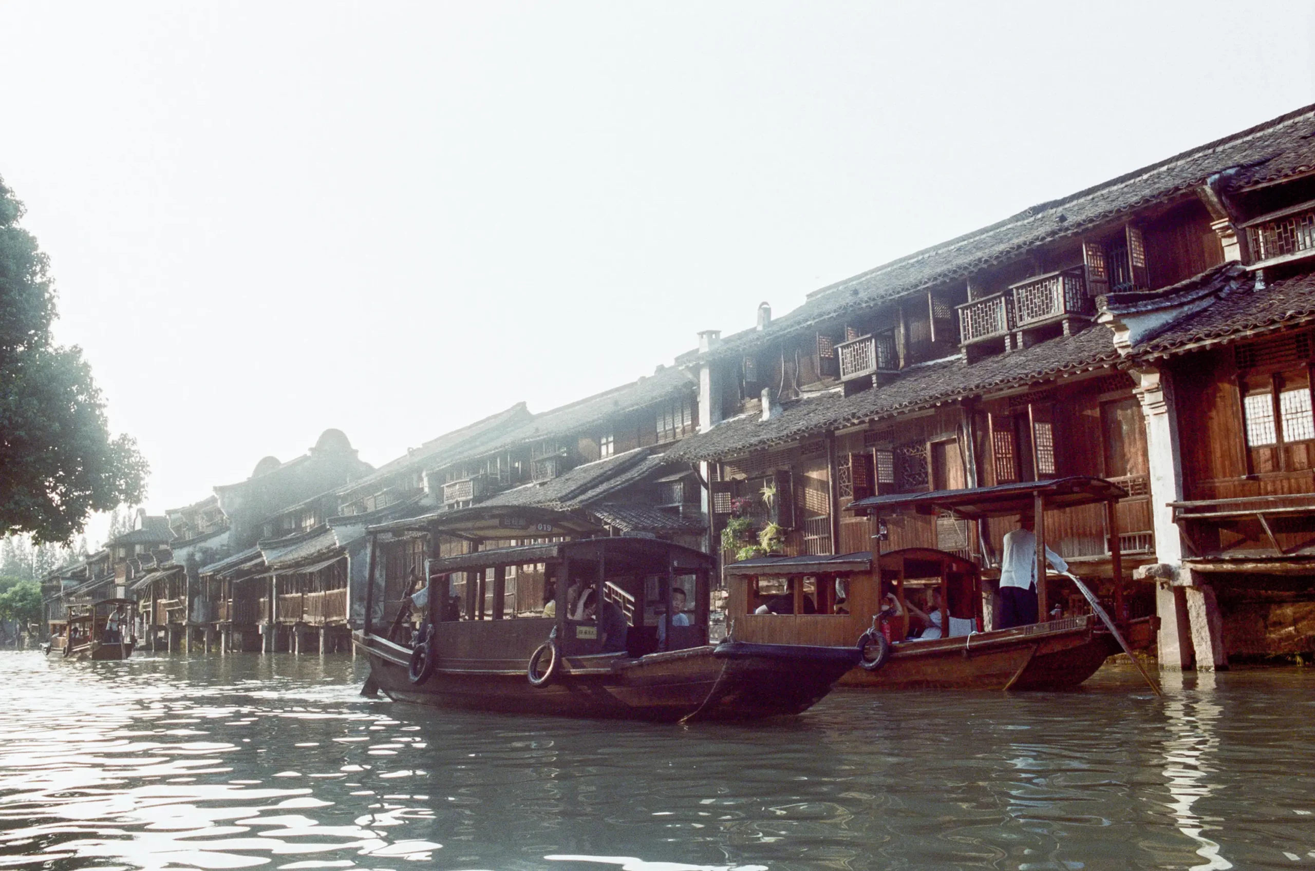 Barques en bois amarrees le long de maisons anciennes au bord d'un canal a Wuzhen, un batelier a la godille