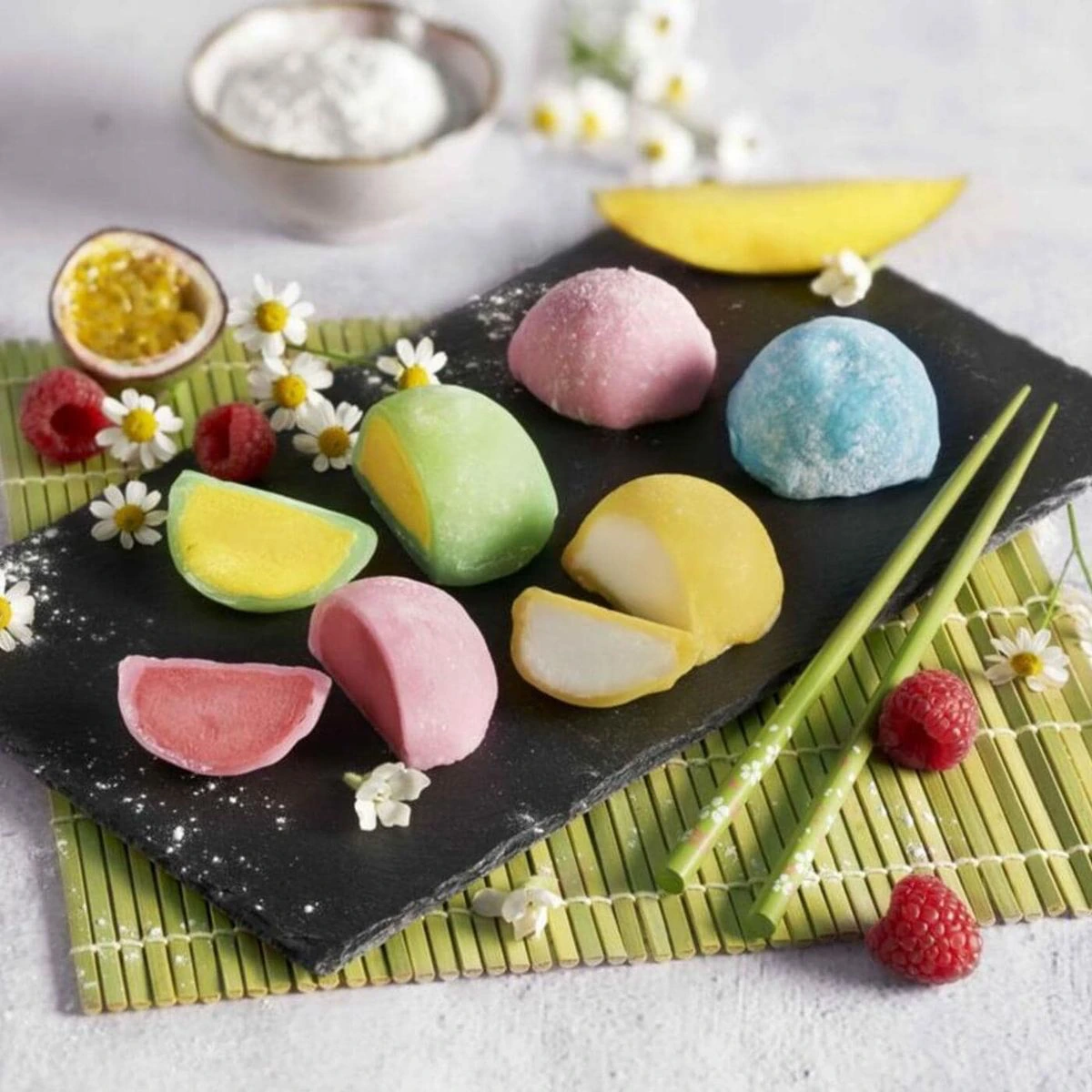 Mochis glaces colores, entiers et coupes, sur une ardoise avec framboises, mangue, fruit de la passion et baguettes